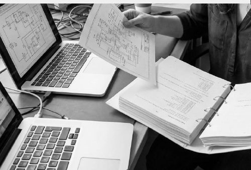 Engineer comparing wiring diagrams next to two laptops